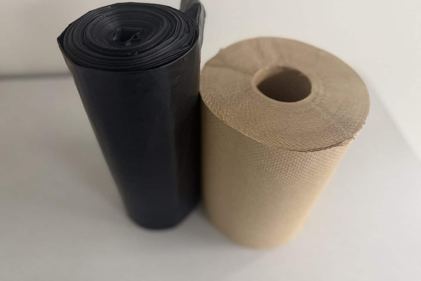 A roll of black can liners beside a roll of brown kraft roll towel
